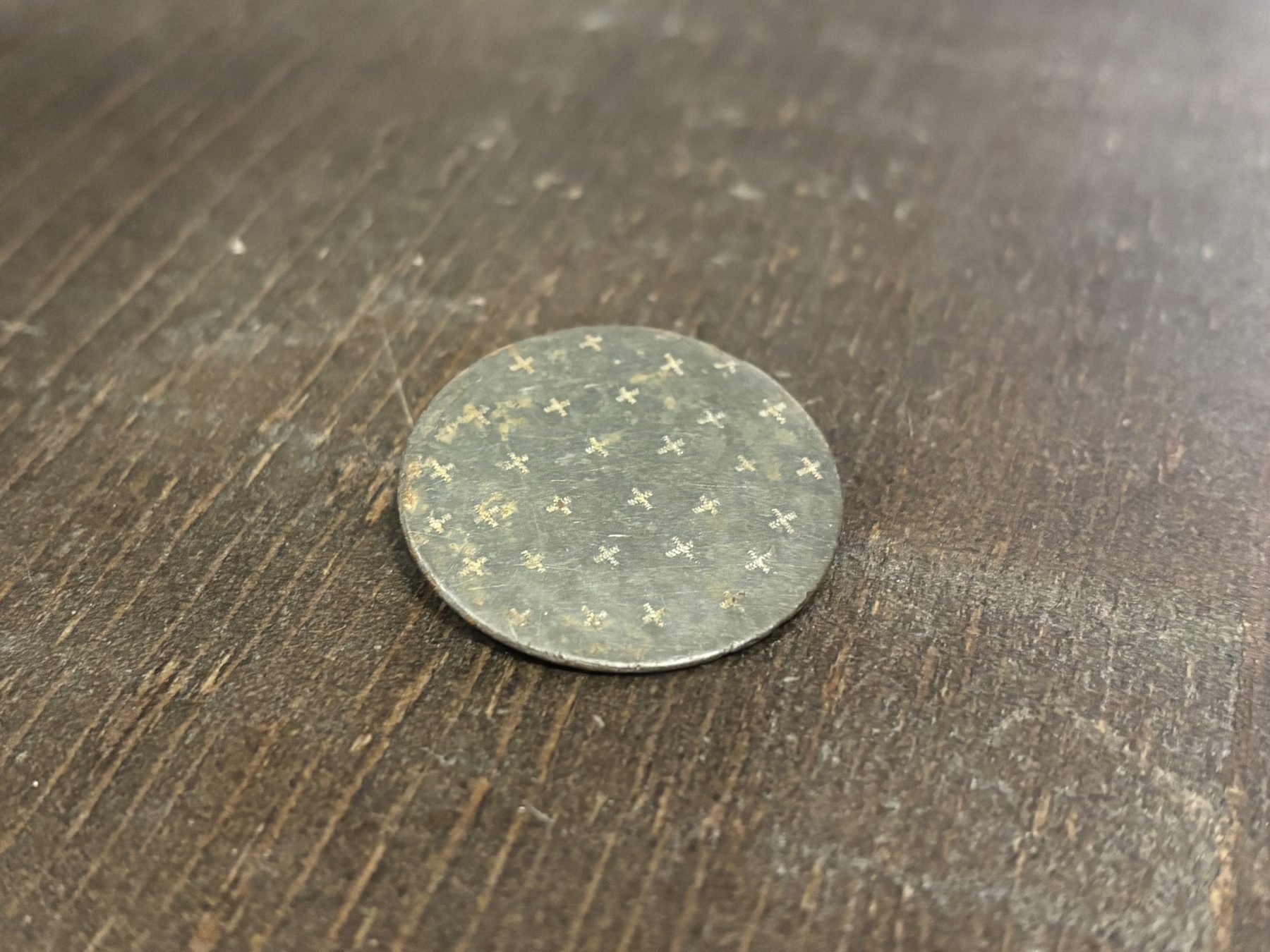 The cleaned button, front face, showing a hand-stamped X pattern